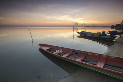 Boats moored in sea against sky during sunset