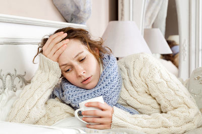 Sick woman holding coffee cup while resting at home