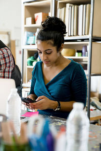 Businesswoman using smart phone while sitting by male colleague