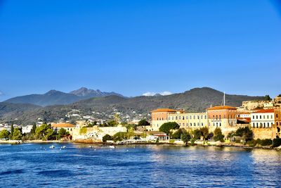 Buildings by sea against clear blue sky