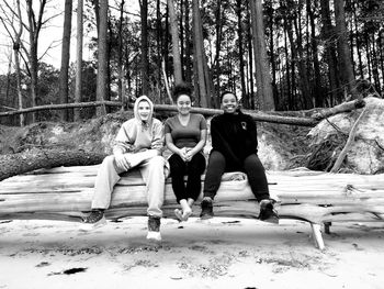 Portrait of smiling friends sitting on fallen tree at beach