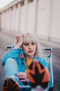 Thoughtful young woman with blond hair sitting in shopping cart