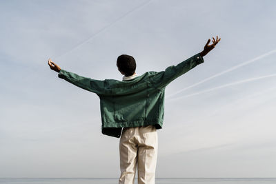 Young man with arms outstretched against sky