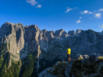 Rear view of person on rocks by mountains against sky