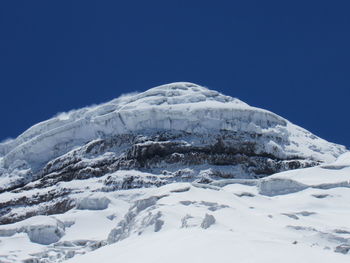 Low angle view of snowcapped mountains against clear blue sky