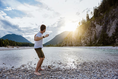 Germany, bavaria, man standing at riverside throwing stone