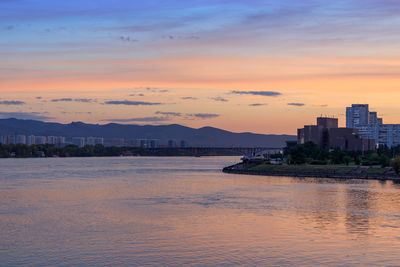 Scenic view of sea by buildings against sky during sunset