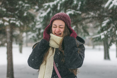 Smiling young woman standing outdoors during snow fall