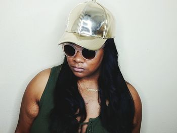 Portrait of young woman wearing sunglasses standing against wall