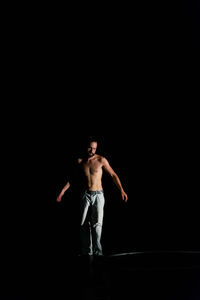 Full length of shirtless man standing against black background