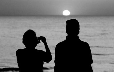 Rear view of silhouette man standing at beach against sky