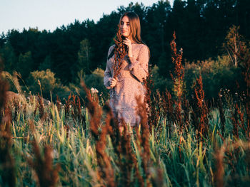 Young woman standing on field against trees