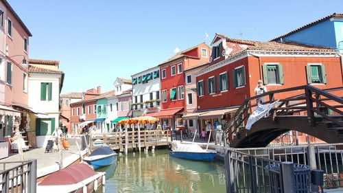 Boats moored in canal by buildings against sky