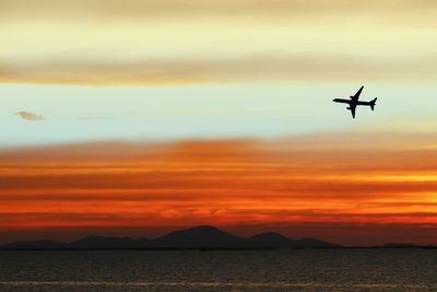 Silhouette airplane flying in sky during sunset