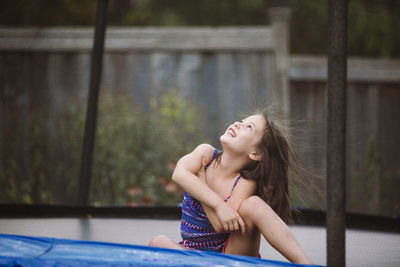 A laughing child with wild hair plays in a trampoline in her yard