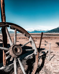 Abandoned wagon wheel on land against blue sky