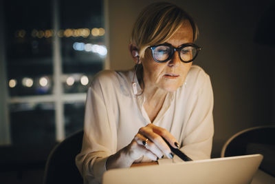 Dedicated mature female professional using laptop in illuminated office while working late