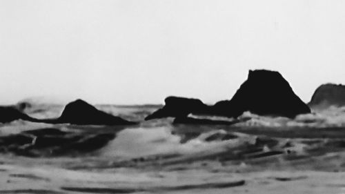 Close-up of silhouette rocks on beach against clear sky