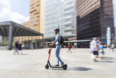 Businessman riding e-scooter on the pavement in the city, berlin, germany