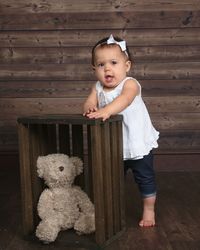 Baby girl standing next to stuffed bear.