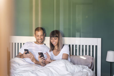 Portrait of smiling young man using smart phone while sitting on bed