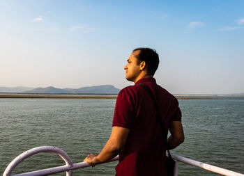 Young man looking at sea against sky