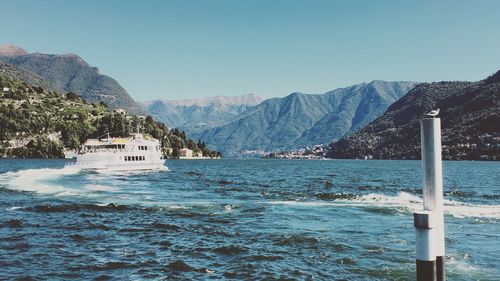 Ferry sailing on sea by mountains against clear blue sky