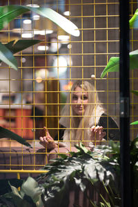Portrait of young woman seen through glass window and metal grate