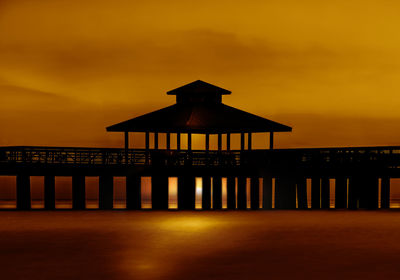 Silhouette built structure by sea against orange sky