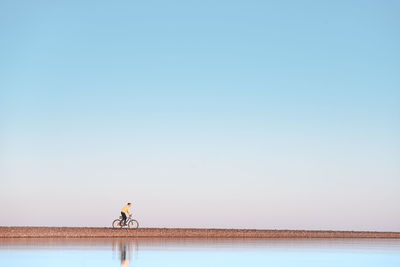 A cyclist rides on a stone spit. the view from the water.