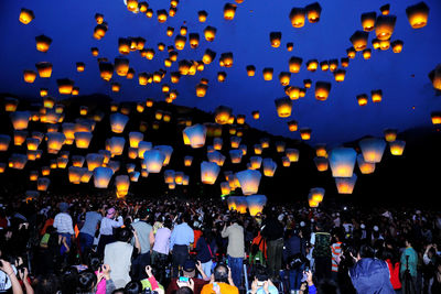 Crowd looking at lanterns in sky at night
