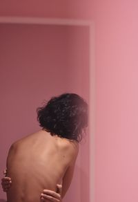 Rear view of shirtless man standing against pink wall