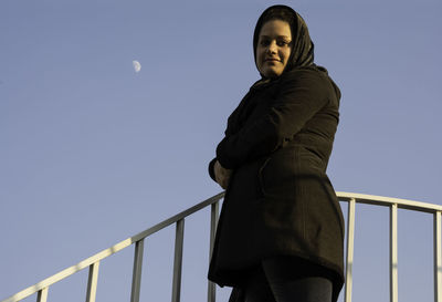 Low angle view of woman standing on railing against clear sky