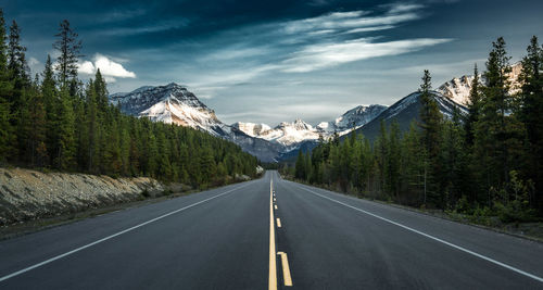 Road amidst trees and mountains against sky