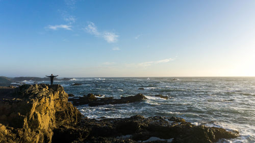 Scenic view of sea with man standing on rock against sky