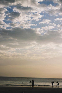Silhouette people on beach against sky during sunset