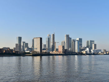 Sea by modern buildings against clear sky