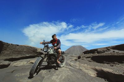 Young man riding motorcycle on desert against blue sky