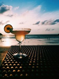 Wineglass on table by sea against sky during sunset