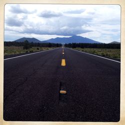 Empty road leading towards mountains against cloudy sky