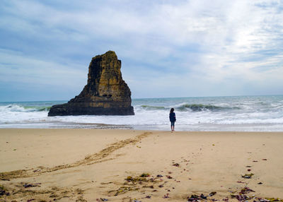 Rear view of person on beach and rock outcropping monolith against sky