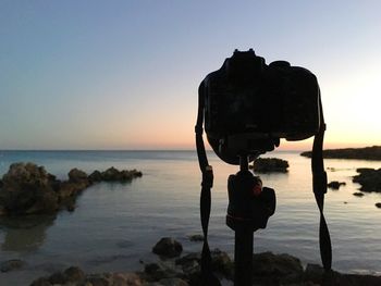 Silhouette rock on beach against clear sky at sunset