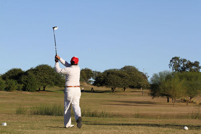 Full length rear view of man playing soccer on field against sky