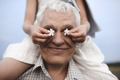 Hands of little girl covering eyes of her grandfather with white blossoms