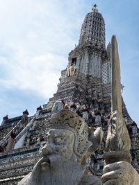 A statue of a guard at the wat arun temple, temple of dawn, in bangkok, thailand, against blue sky.