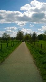 Dirt road amidst field against sky