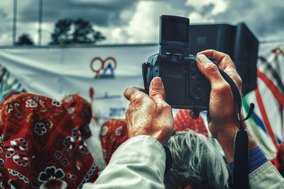 Low section of man holding camera against sky