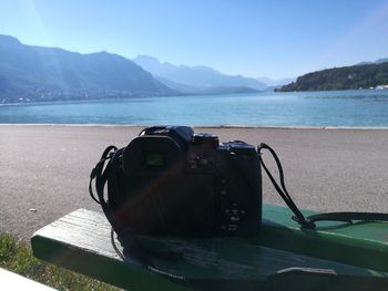 Digital camera on bench at lakeshore against clear blue sky