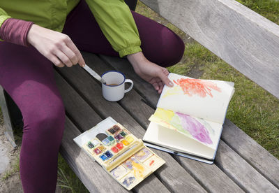 A woman draws a sketch with watercolors in a notebook in the open air and drinks