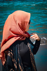 Midsection of woman holding umbrella while standing by sea